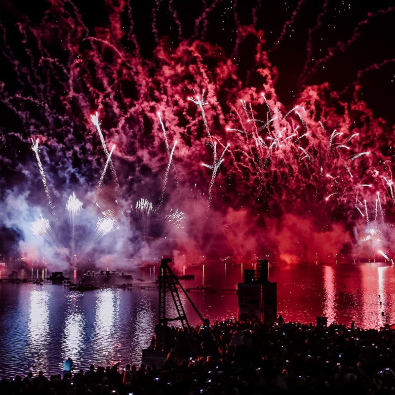 Beleuchtetes Feuerwerk auf einem Event, davor ein See bei Nacht